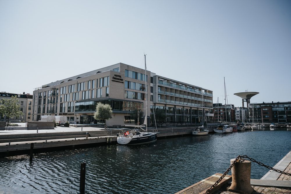Modern waterfront building complex with boats docked along a marina in an urban harbor setting.