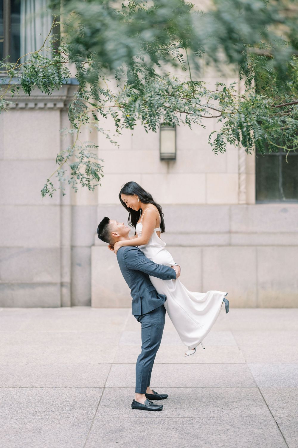A romantic couple pose with a joyful lift against an elegant building exterior.