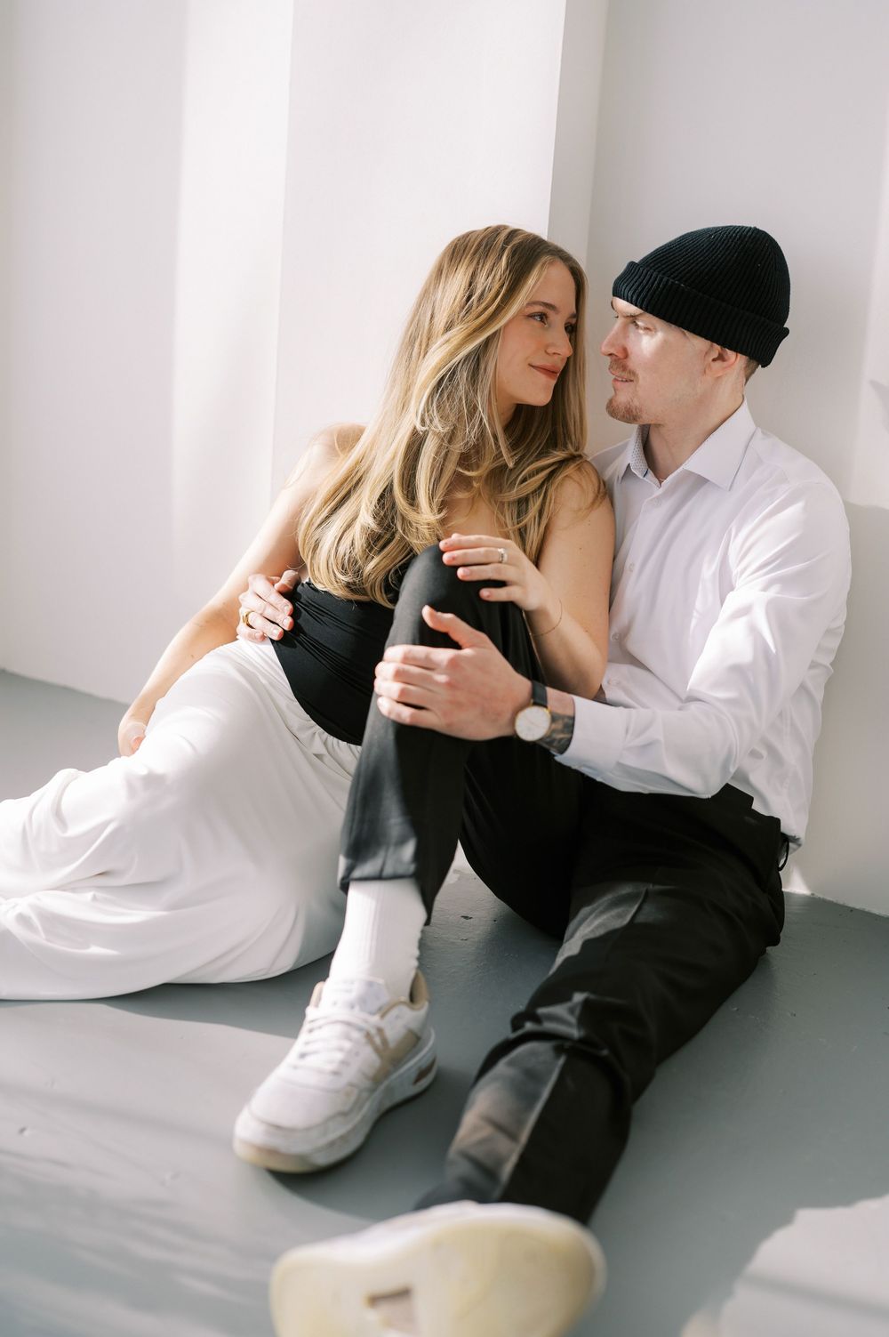 Two people share an intimate moment sitting on the floor against a white wall while dressed in contrasting black and white.