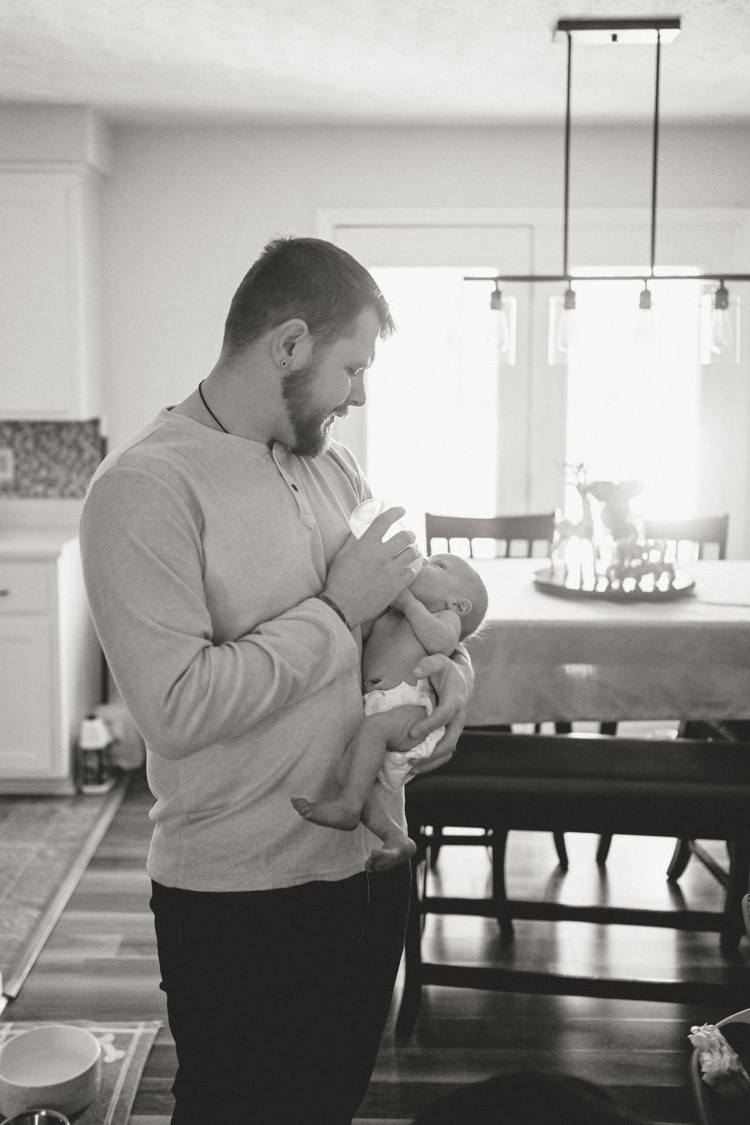 Black and white image of dad bottlefeeding baby boy during lifestyle newborn session in Clarksville, Tennessee by Disney Magic Photography