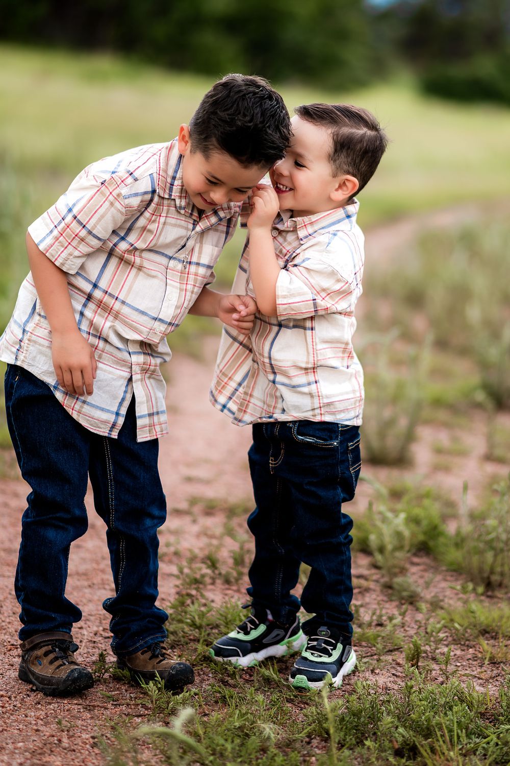 Two people in matching plaid shirts and jeans share a playful moment together on a dirt path outdoors.