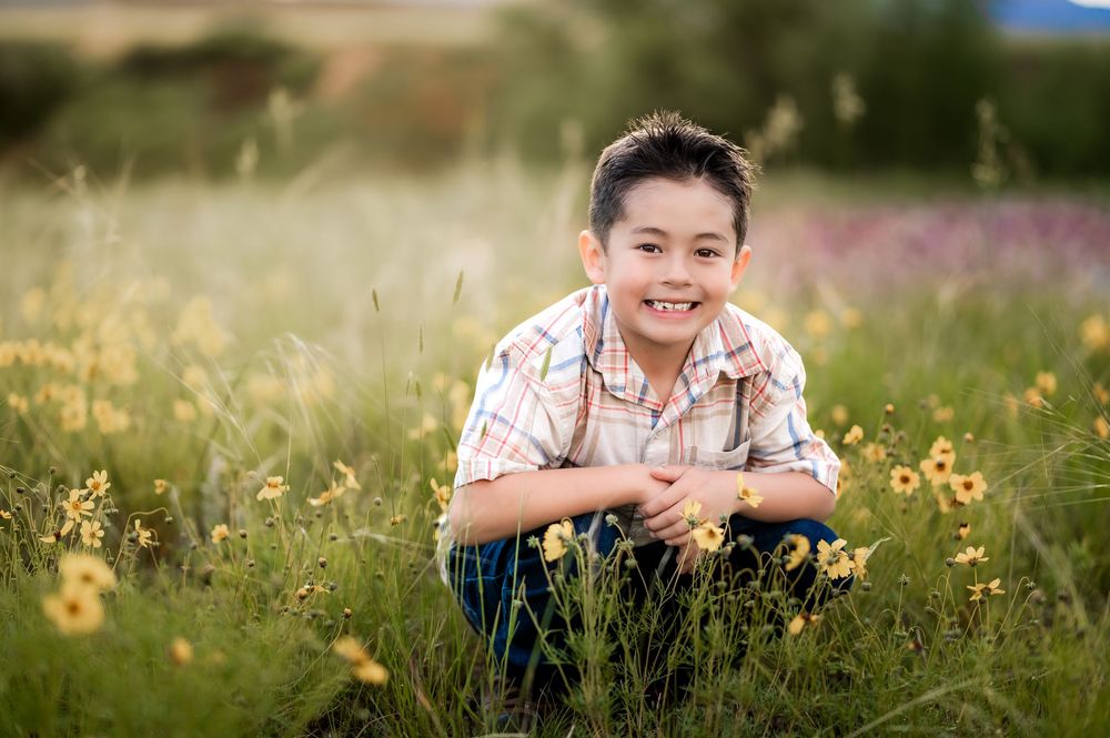Someone sits in a field of yellow wildflowers while smiling during a golden hour outdoor photoshoot.