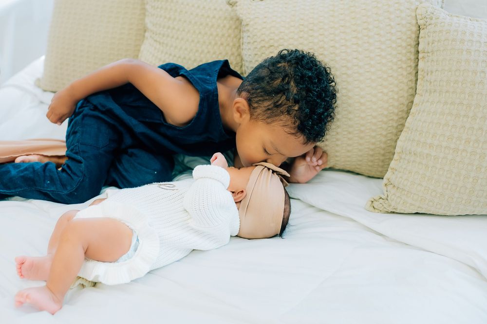 Siblings sharing a sweet moment on a white couch with decorative pillows.