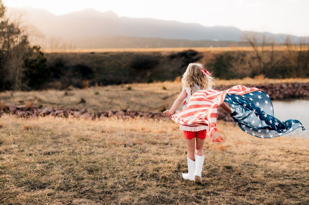 American flag flowing in the wind against mountain landscape at sunset.