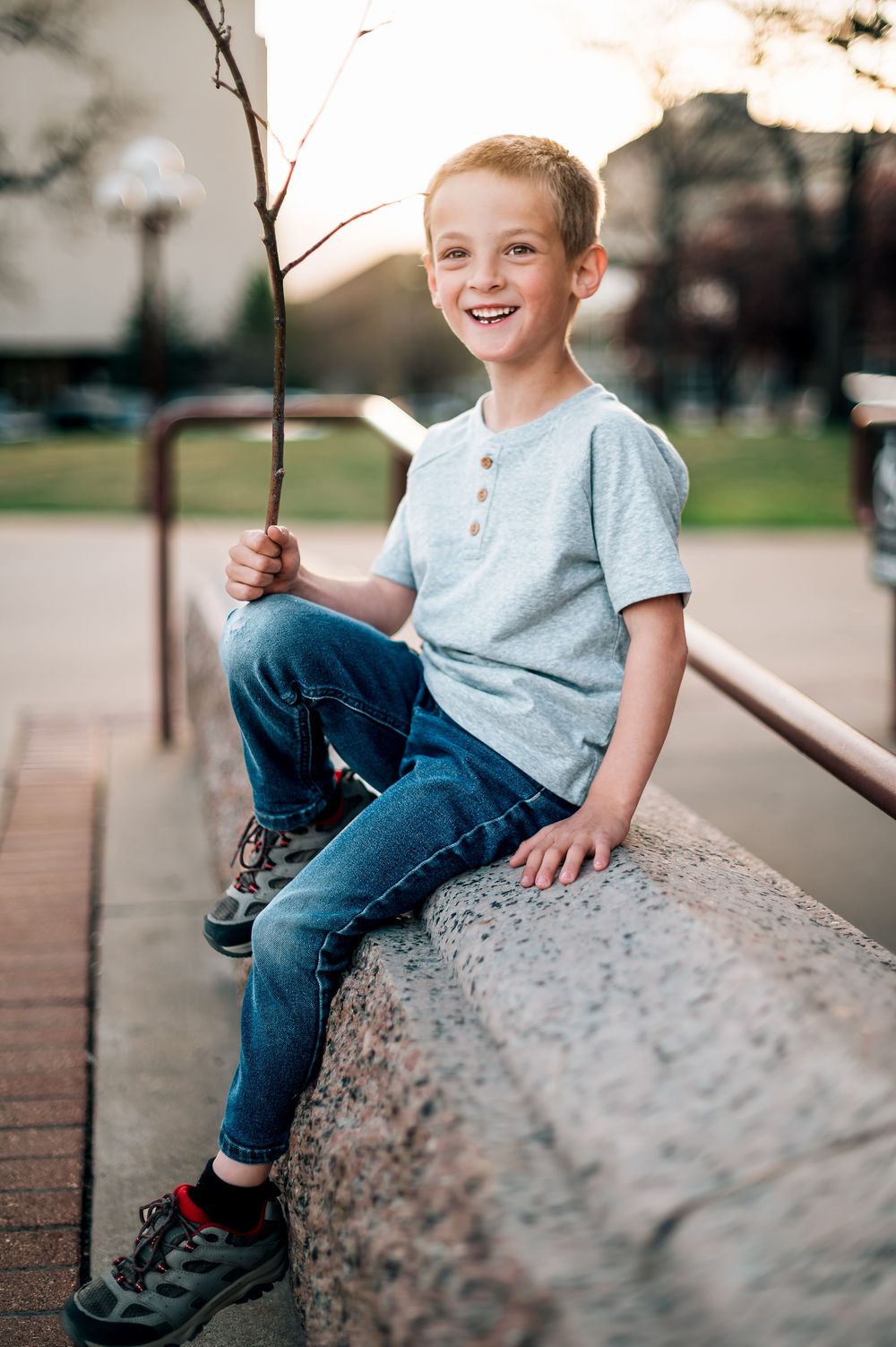 A casual outfit featuring jeans and blue shirt shown on a stone wall during sunset.