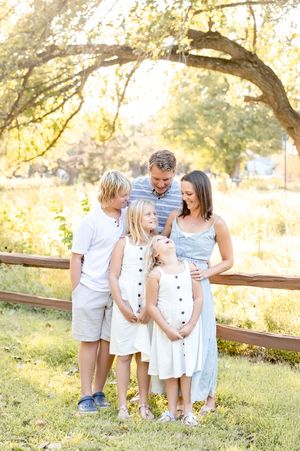 A family stands together by a rustic wooden fence in a sunlit park during golden hour.