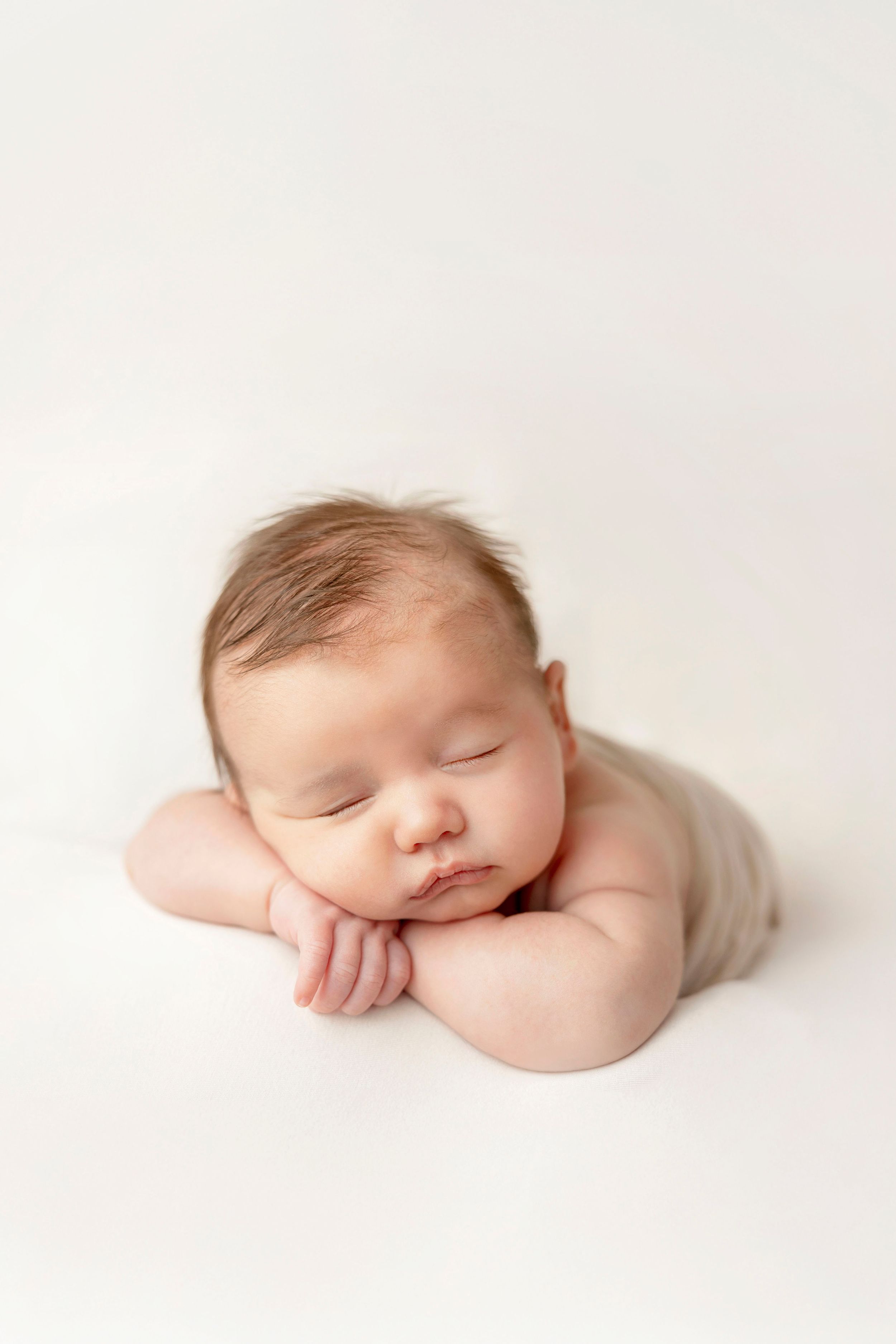 Peaceful sleeping newborn baby in soft white wrap photographed in minimalist style against white background.