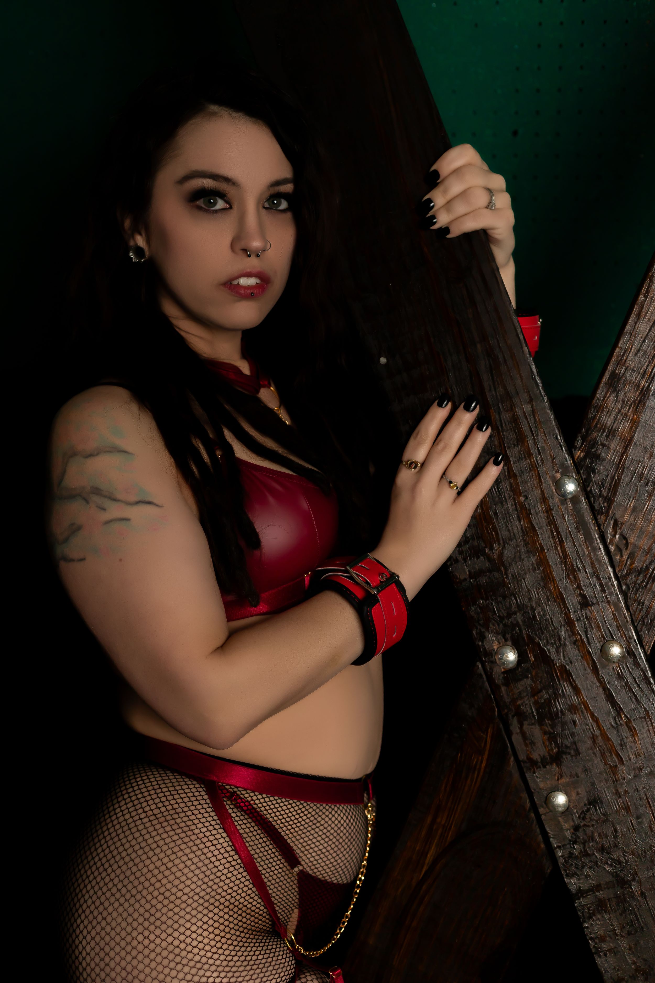 Dark and moody photo of someone in red lingerie holding a guitar against a deep green background.