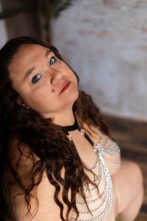 Portrait of someone in elegant pearl necklace and choker with long dark curly hair against blurred background.
