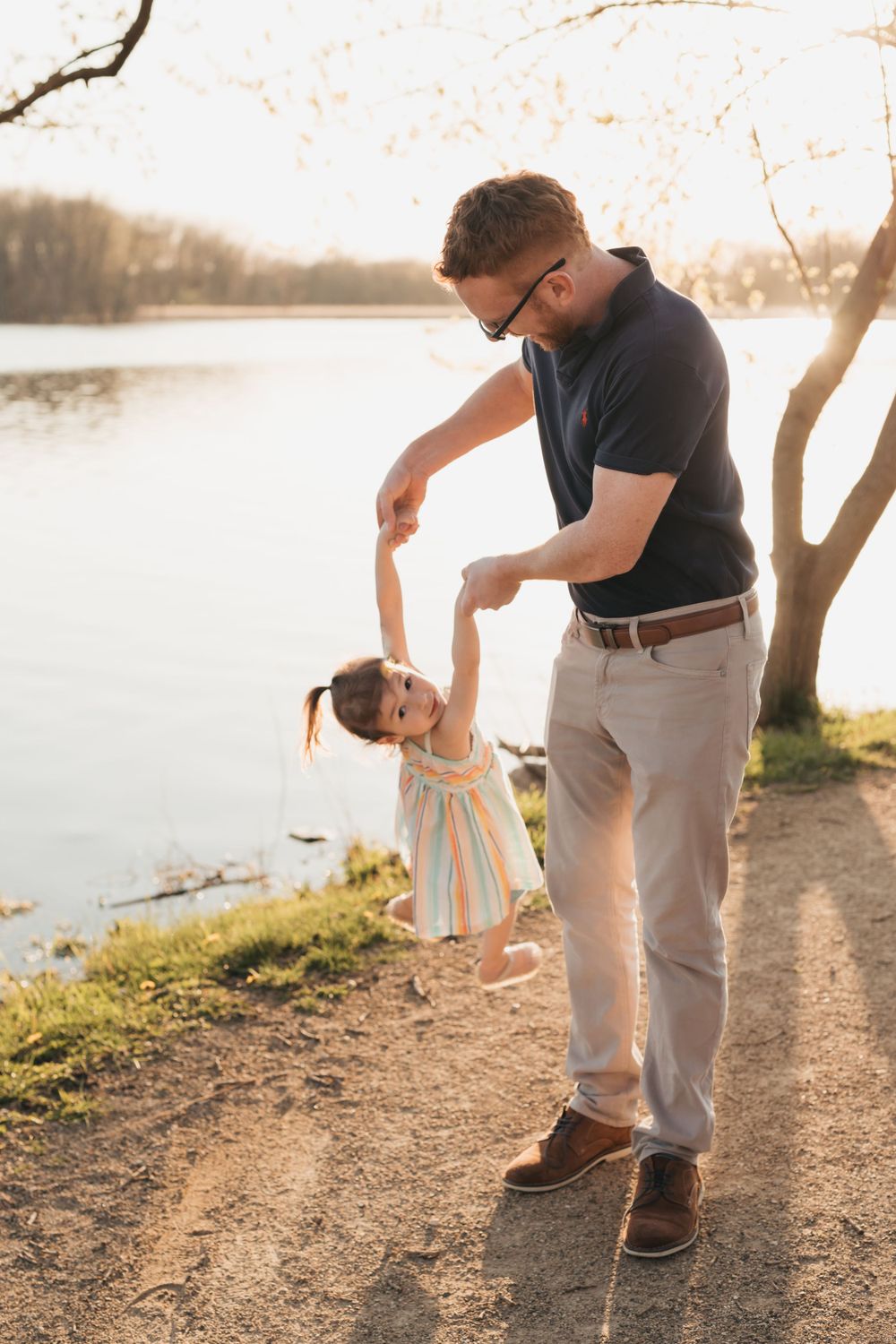 Sweet bonding moment along a lakeside path at sunset, captured in warm glowing light as they dance together.
