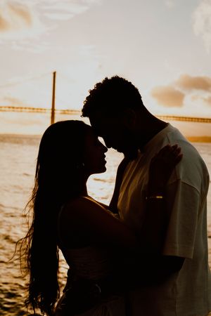 Silhouetted couple embracing on beach at sunset with warm golden light creating romantic atmosphere.