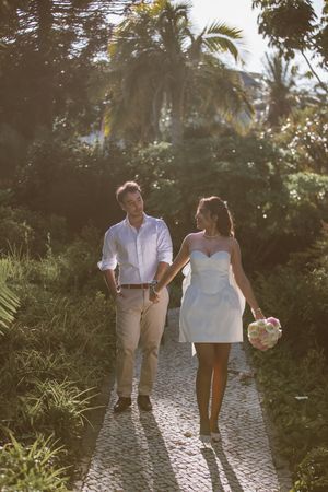 A couple walking hand in hand on a stone path through a lush tropical garden at sunset.