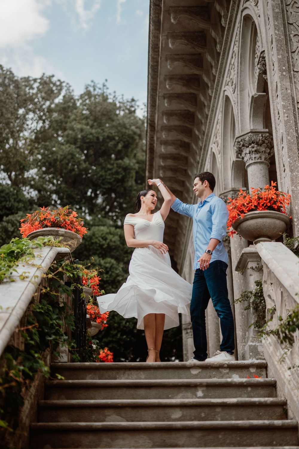 Romantic couple dancing and posing together on stone steps with red flowers and ornate architectural details.