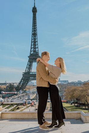 A couple poses together in front of the iconic Eiffel Tower in Paris on a sunny winter day.