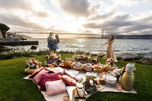 Romantic beach picnic setup with blankets, pillows and charcuterie spread along the oceanfront at sunset.