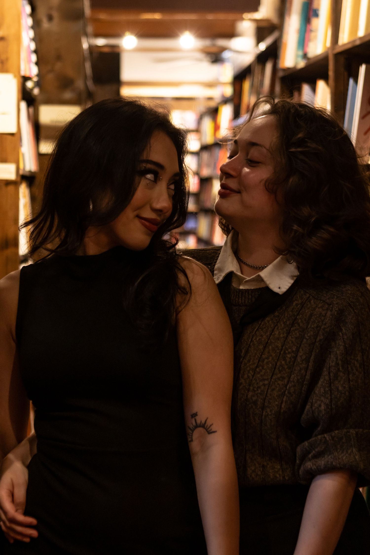 A sapphic couple checks out books together, and makes eyes at each other in a shop in downtown Ashland