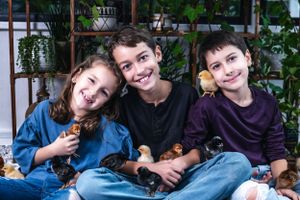 Three siblings sitting together holding small pets and smiling.