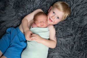 Two children cuddling on soft gray fur blanket during newborn photoshoot.