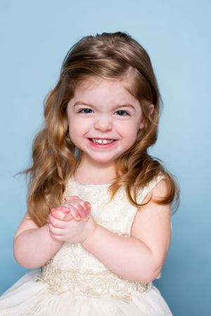 Young girl in cream dress smiling brightly against light blue background.