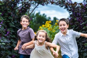Three kids running and playing together in blooming summer garden.