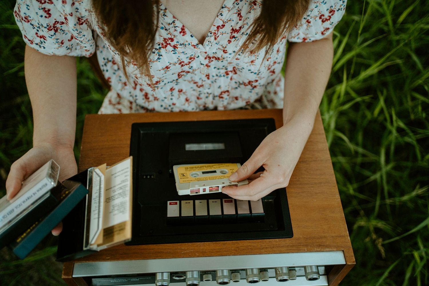 Hands arranging items in a leather-bound book on wooden surface outdoors.