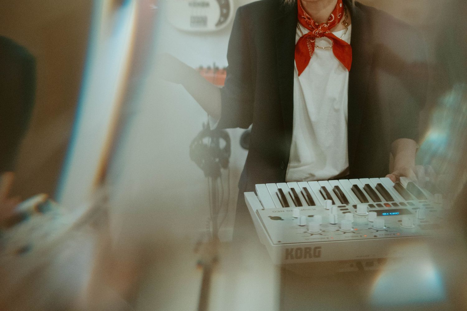 Musician playing a Korg synthesizer keyboard while wearing a red scarf and black blazer during a live performance.