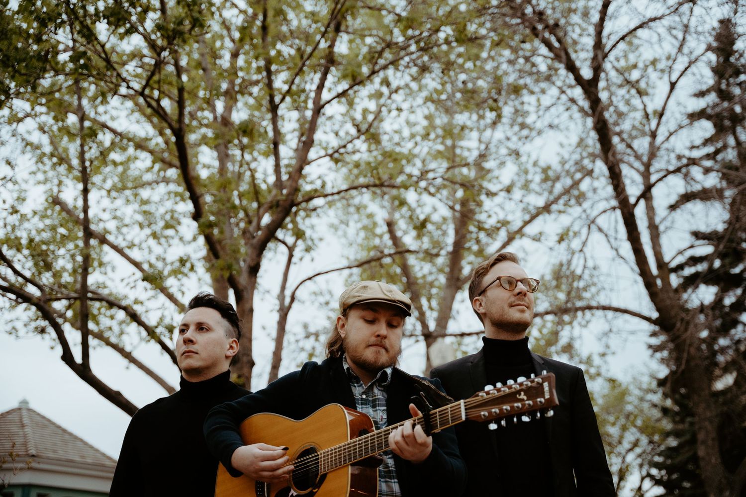 Three musicians performing outdoors with an acoustic guitar against an autumn backdrop.