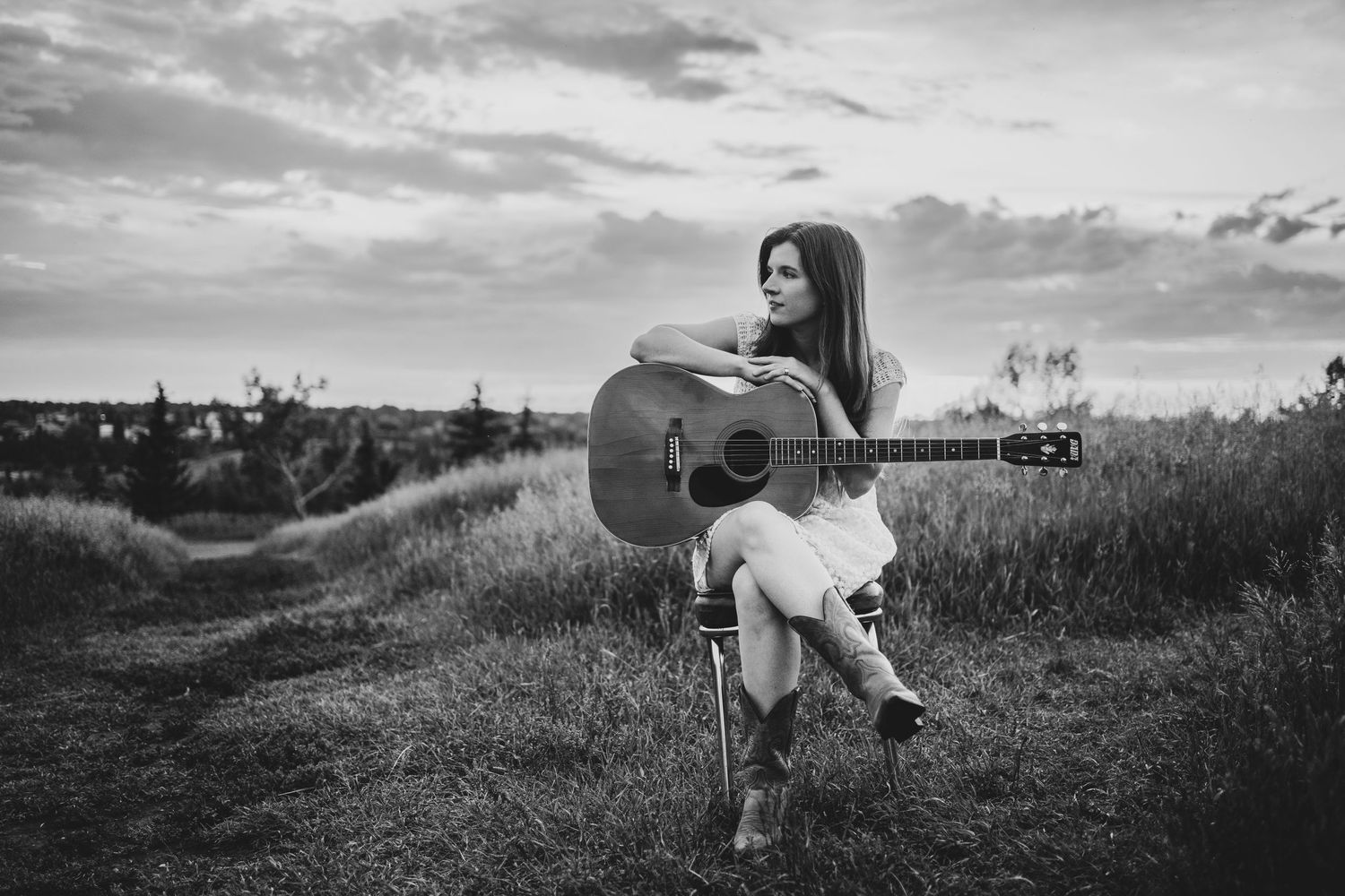 Musician sitting in a grassy field at sunset with an acoustic guitar.