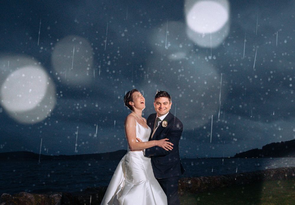 Couple dancing in the rain at night with bokeh lights and moonlit sky.