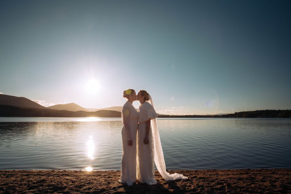 Romantic sunset silhouette of couple by lakeside in wedding attire.