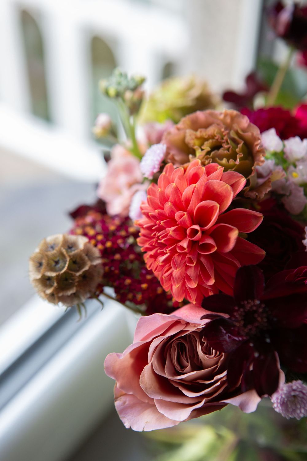 Close-up of a vibrant floral arrangement featuring pink dahlias and roses by a window.