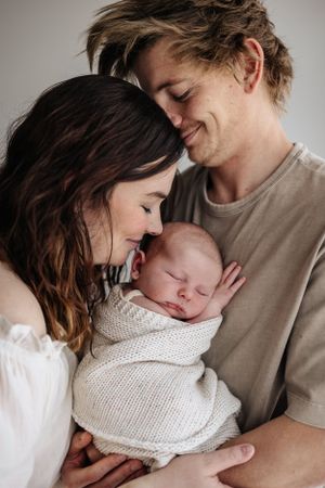 Loving parents share an intimate moment with their newborn baby wrapped in a cozy knit blanket.