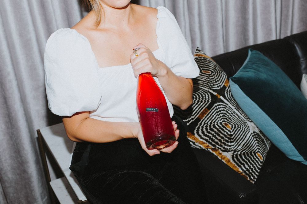 Someone sitting on a patterned couch holding a red drink.