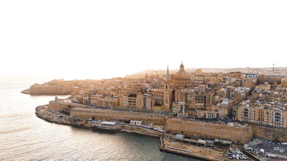 Drone photo of Malta coastline at sunset with golden light over historic city and Mediterranean Sea