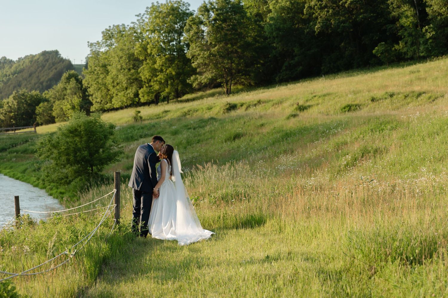 Bride and groom share a romantic kiss in a golden field, with her veil billowing in the wind.