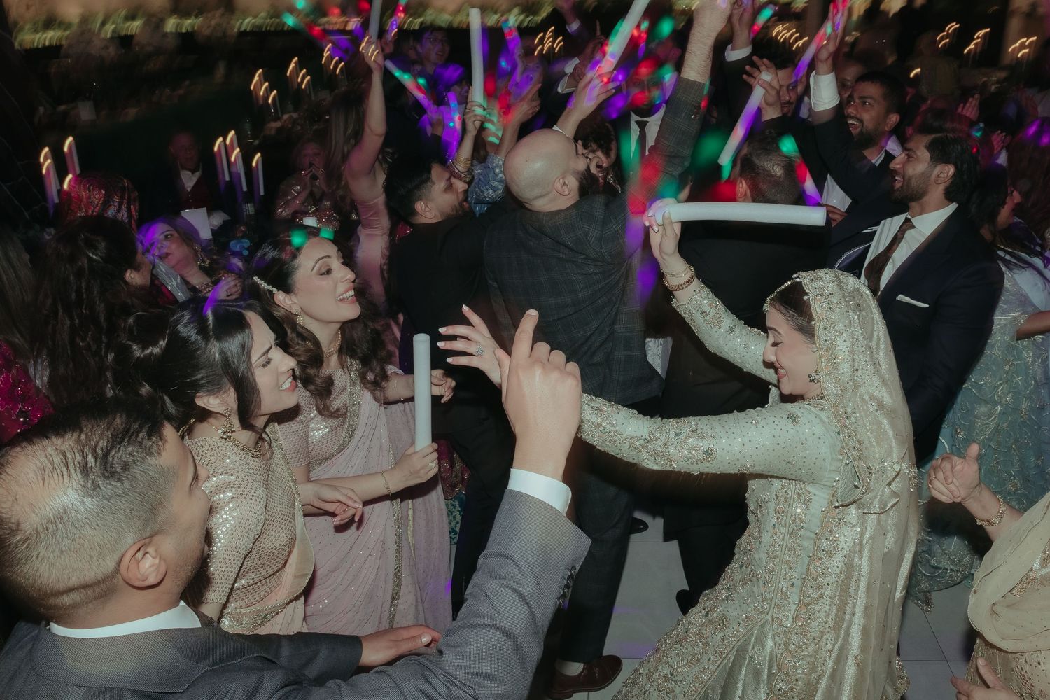 A joyful wedding moment captured in sepia tones shows a group of people in elegant traditional dress sharing laughter together.