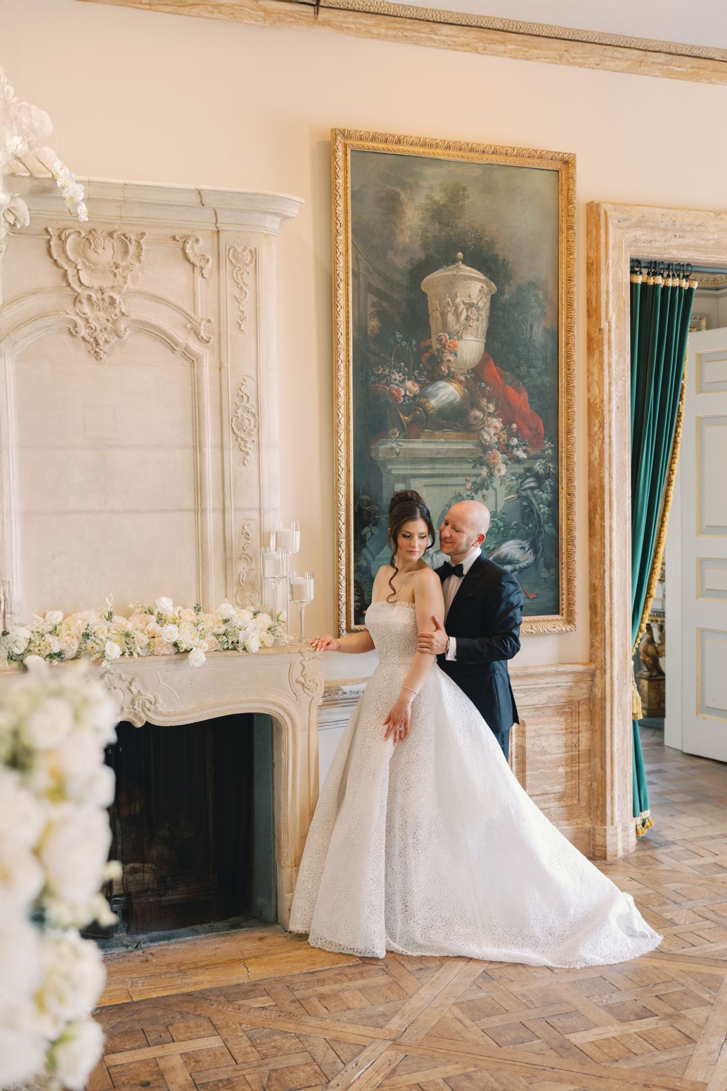 Bride and groom posing by ornate fireplace in elegant French chateau wedding venue.