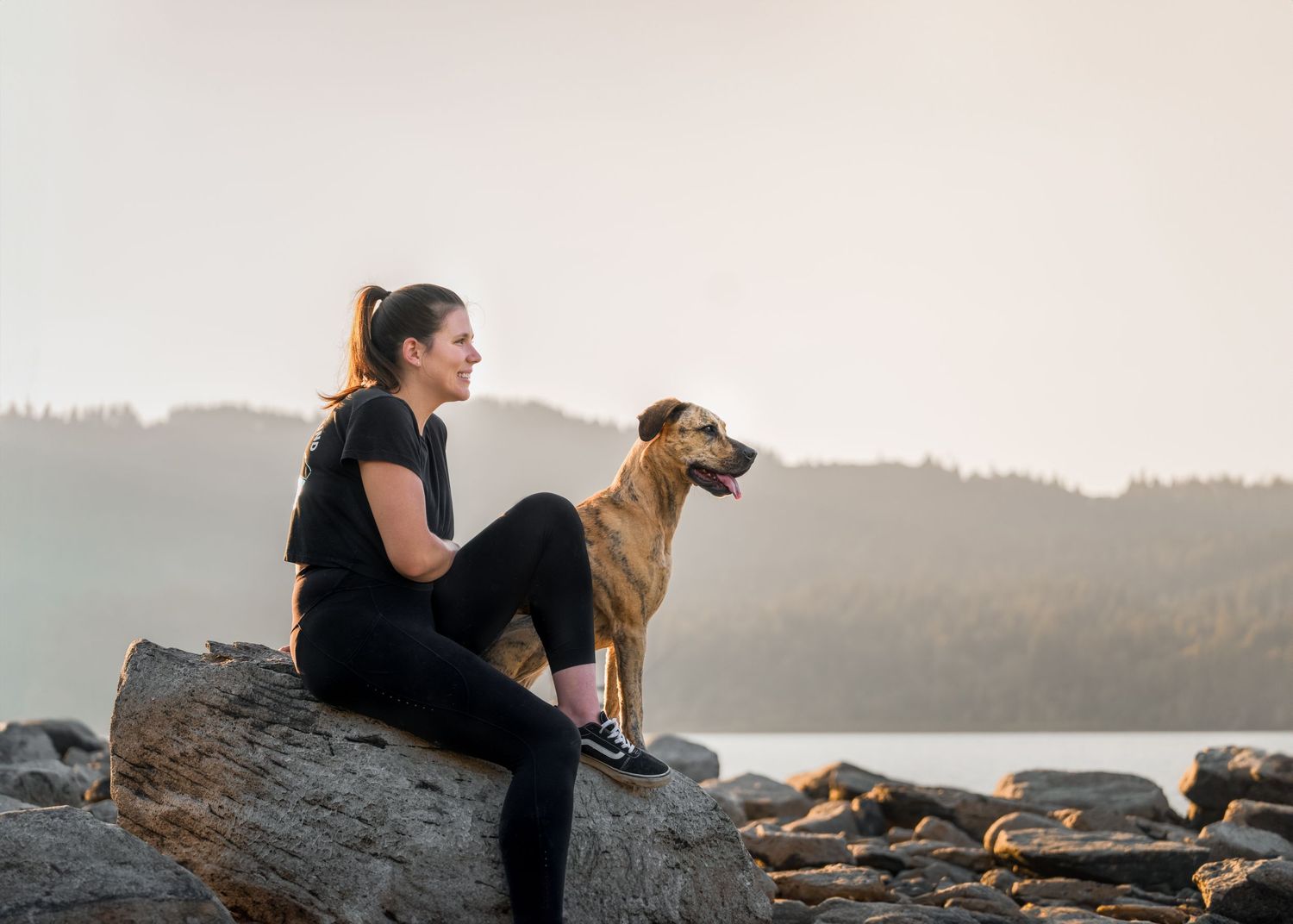 catahoula brown dog sitting with her female owner at the beach, river, water, Boulders, sunset, misty rays, forest hill