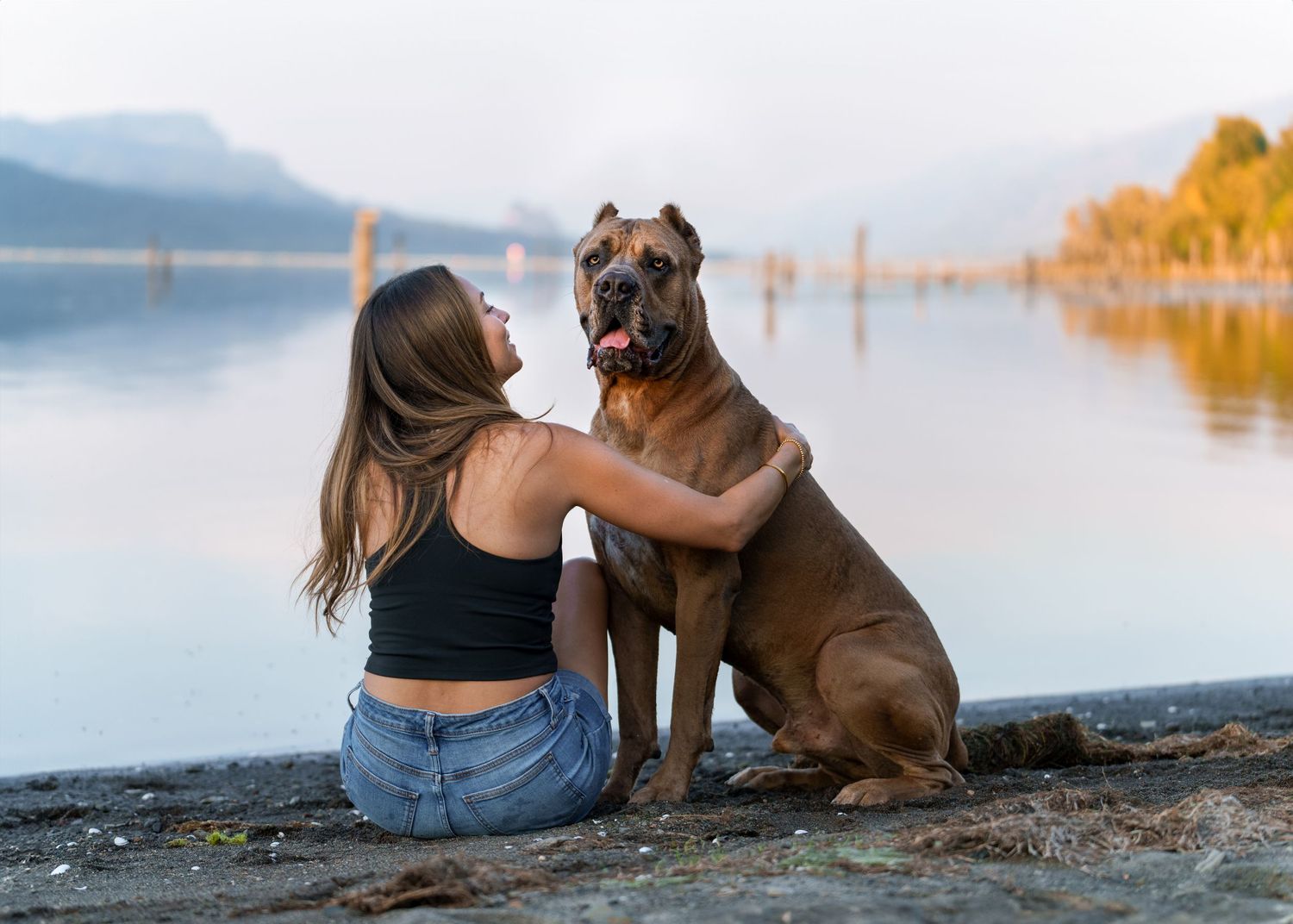 woman and corso dog portrait by the river with mountain views, water, sunset