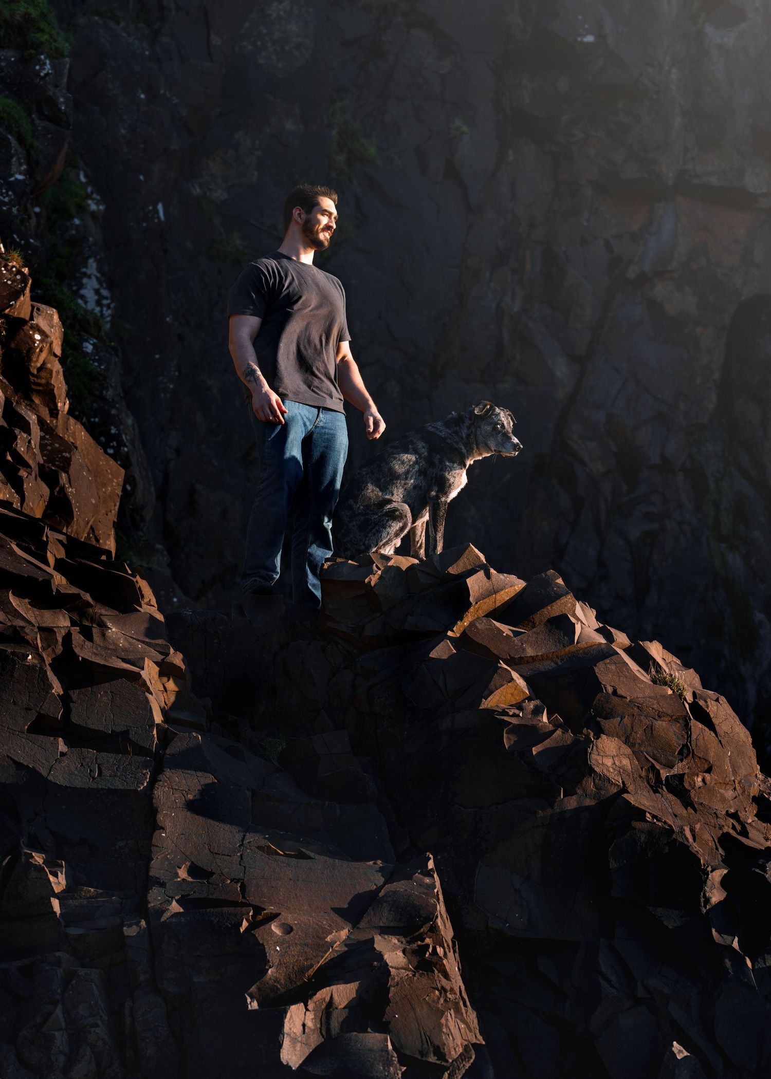 man standing on top of the cliff with the dog, sunset, rustic