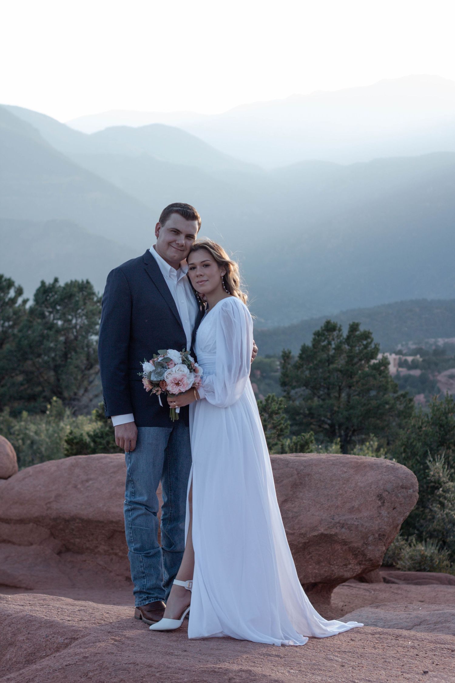 A wedding couple poses elegant together on red rocks at Garden of the Gods with misty mountain views in the background.