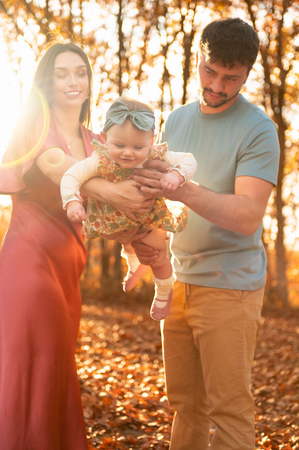 Family of three enjoying a tender moment in autumn forest with golden sunlight streaming through trees.