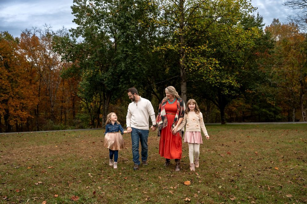A group of people walk together through an autumn field surrounded by colorful fall foliage.