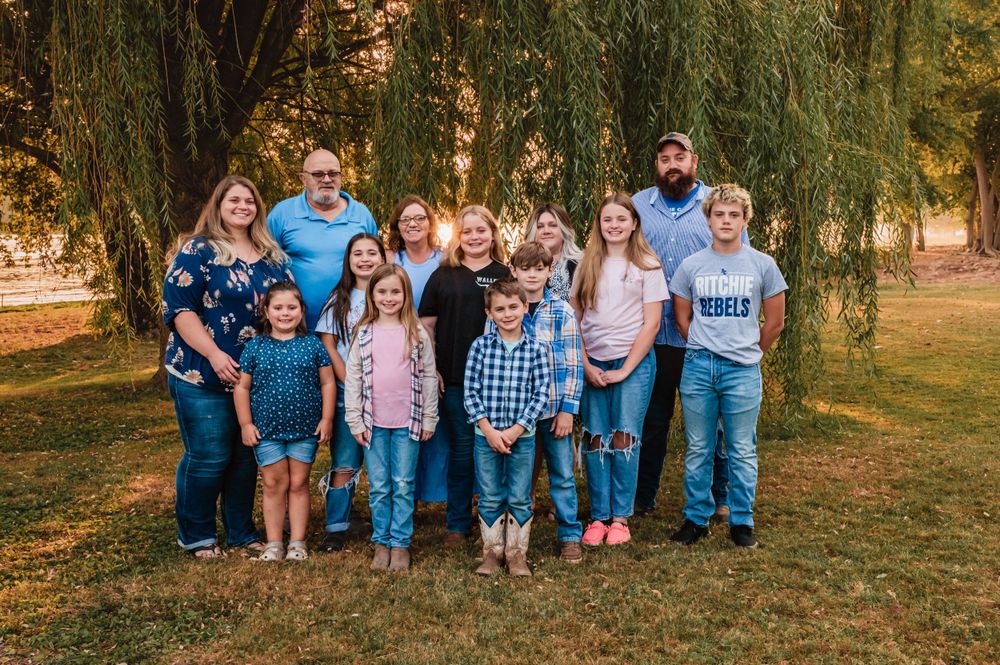 Extended family group portrait under weeping willow trees at sunset.