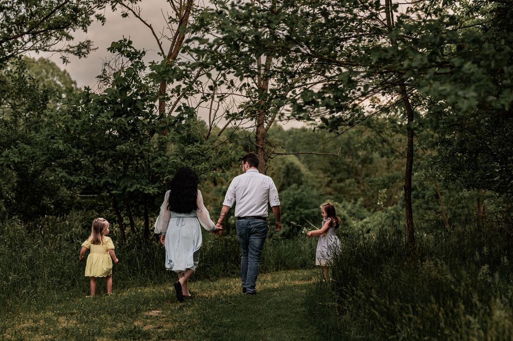 Family walking together on nature trail through lush green trees at sunset.