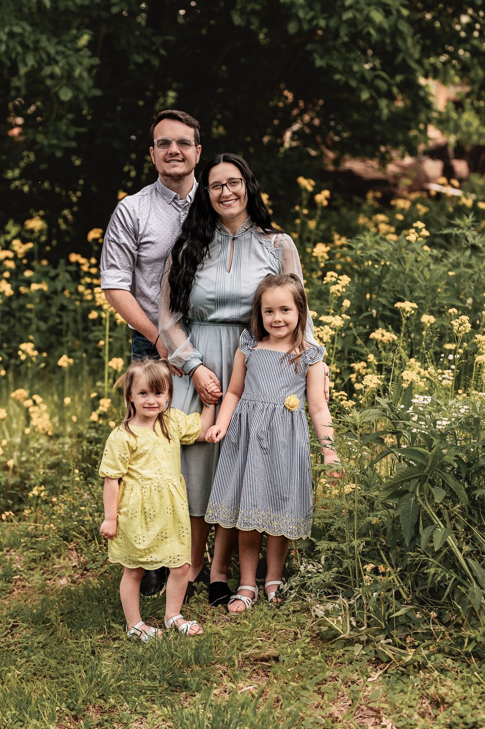 Portrait of young family with two children standing in garden with yellow flowers.