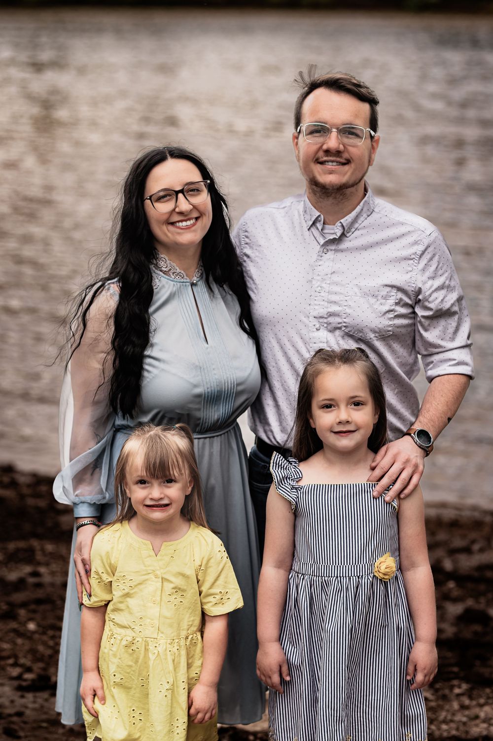 Outdoor family portrait against brick wall showing parents with two young children.