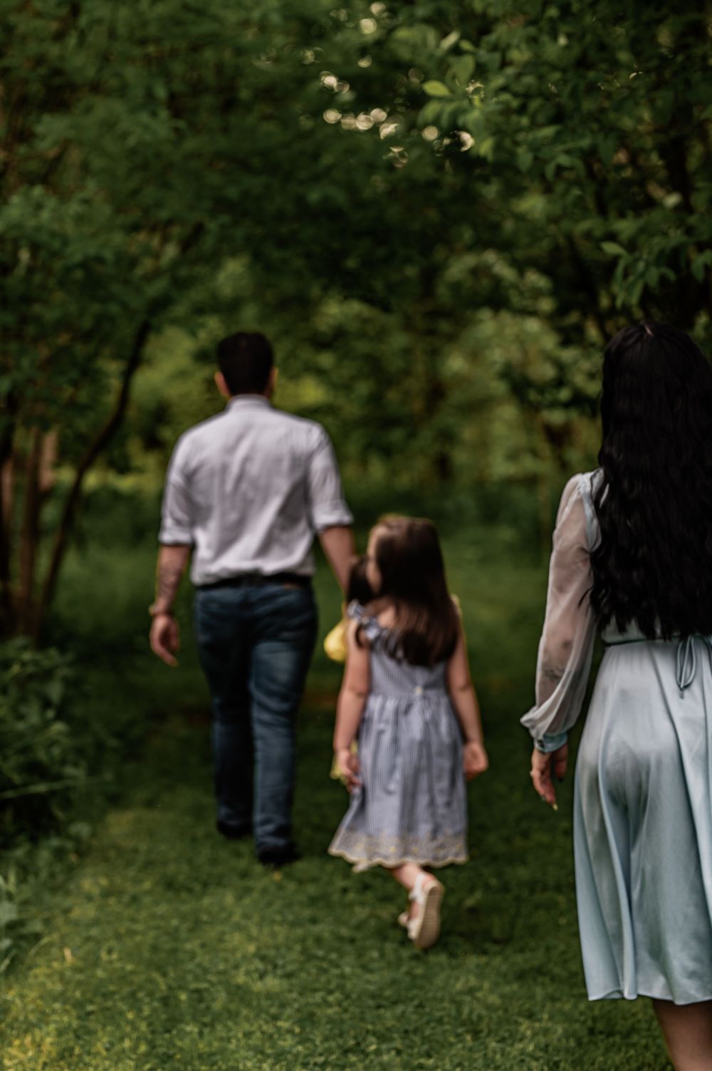 Family walking along a green nature path with adults and a child in summer dresses and casual wear.