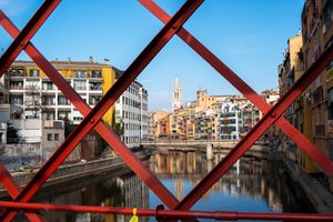 Red metal bridge structure frames a European canal and architecture photographed by Gia Quilap.