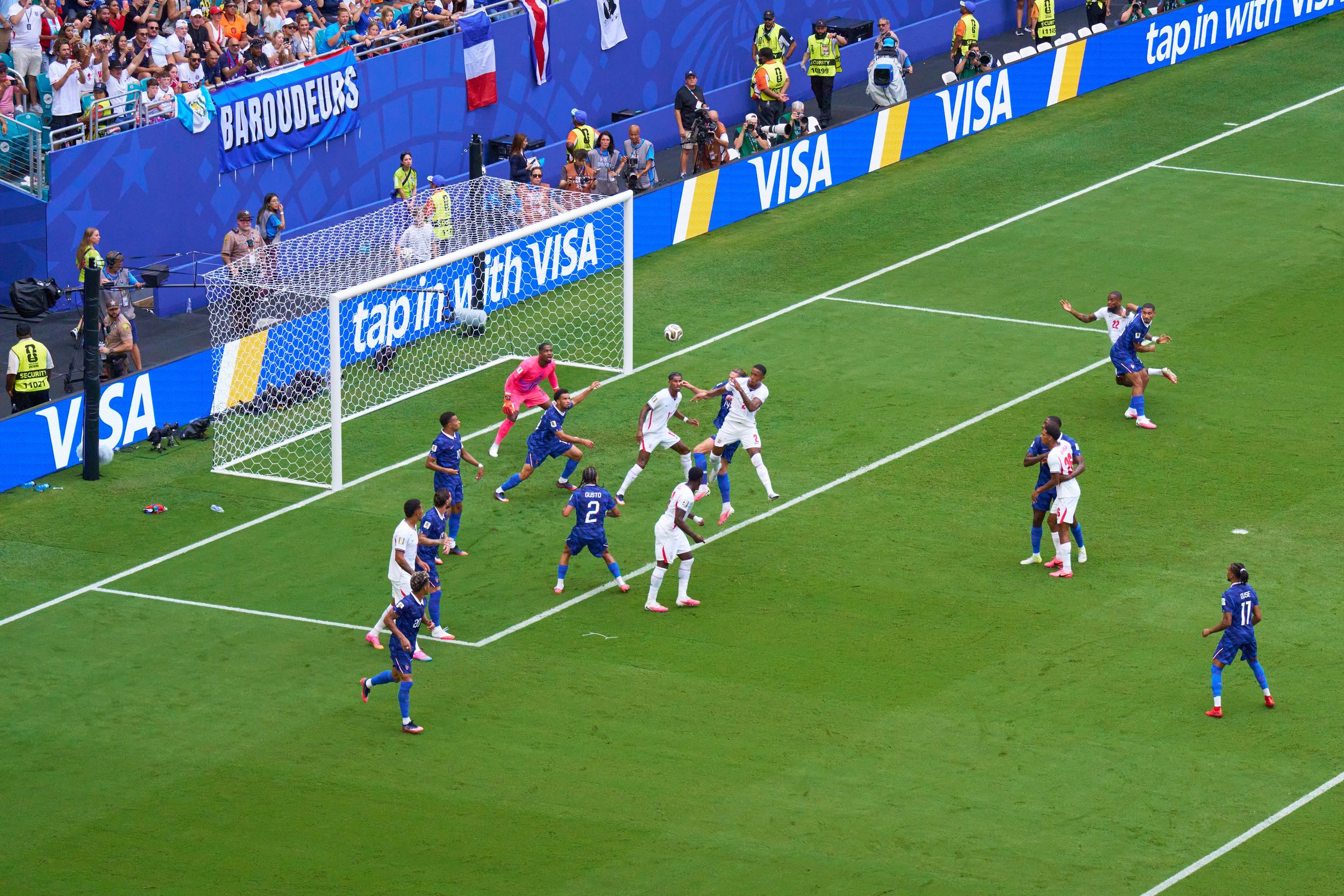 Soccer players compete near the goal during a FIFA World Cup match with VISA advertising boards visible.